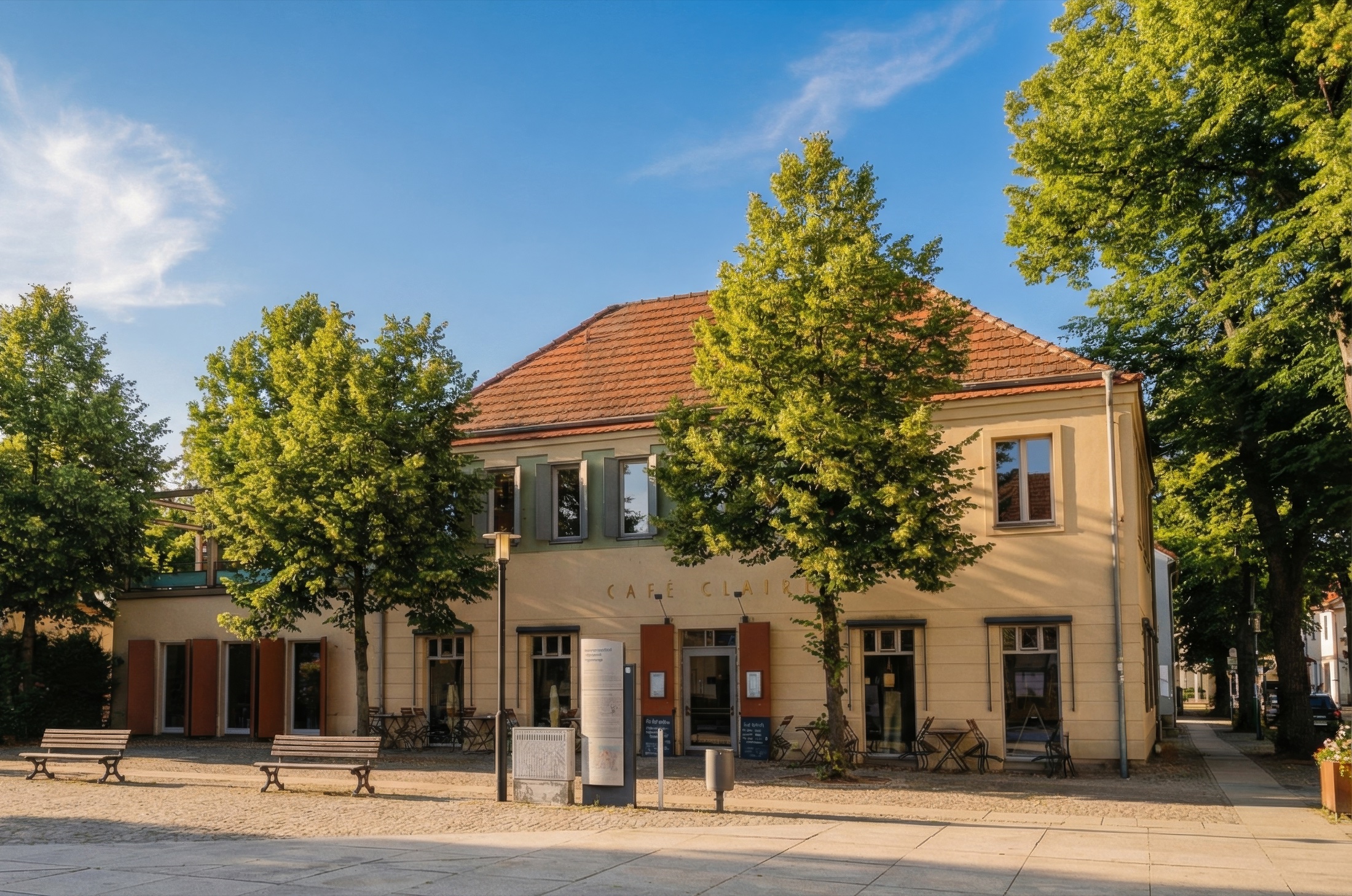 Die helle Fassade des Café Claire unter den Bäumen am Kirchplatz in Rheinsberg